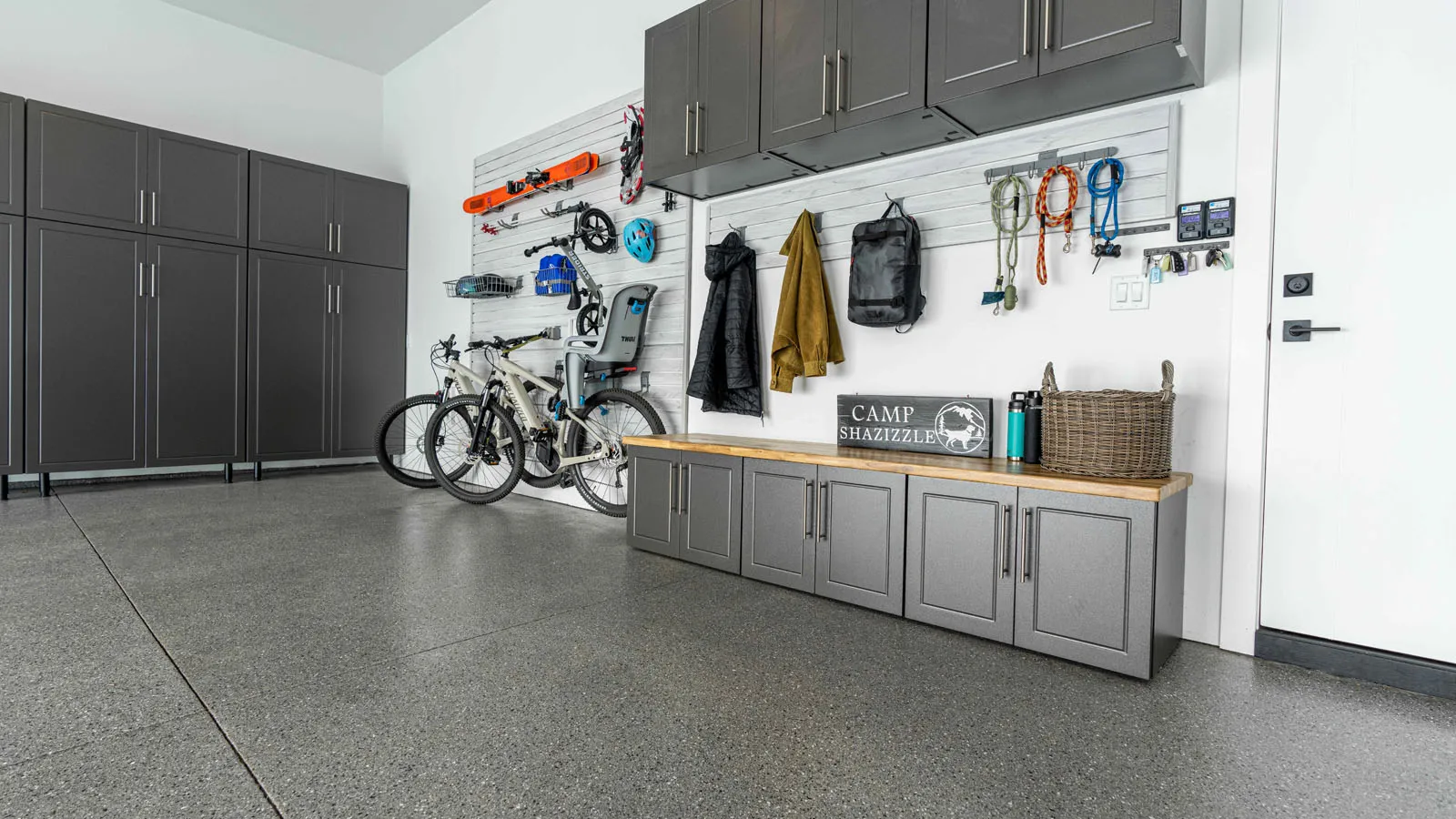 Modern garage with custom gray cabinetry, wall-mounted storage for bikes and gear, and built-in bench—garage cabinetry provided by Spearfish Building Supply in Spearfish, SD.