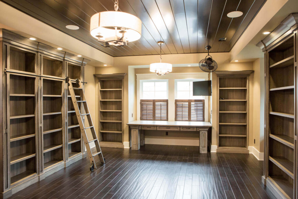 Custom-built home office with floor-to-ceiling wooden bookshelves, a rolling ladder, built-in desk, and rich dark wood flooring—highlighting detailed interior millwork craftsmanship available from Spearfish Building Supply.