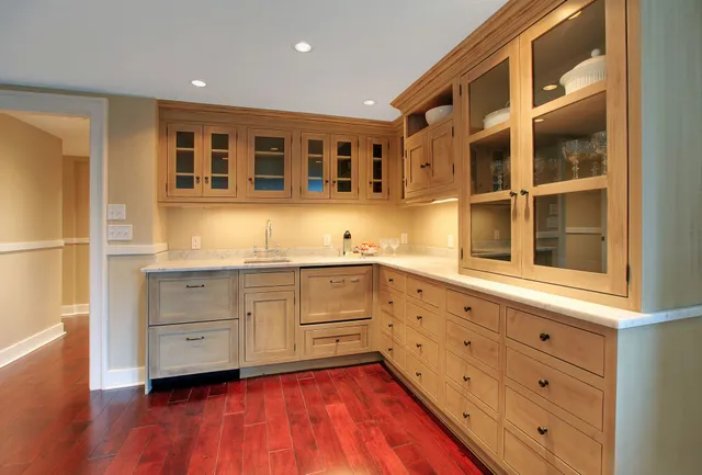 Custom millwork kitchen featuring natural wood cabinetry with glass-front upper cabinets, built-in drawers, marble countertops, and rich hardwood flooring—showcasing craftsmanship available through Spearfish Building Supply.
