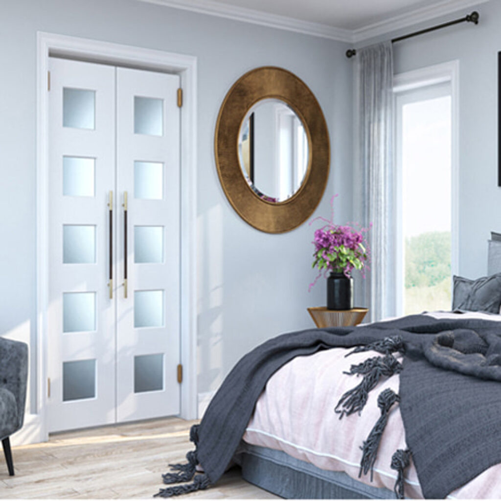 Modern bedroom featuring stylish white double interior doors with frosted glass panels and brass handles, alongside a round gold-framed mirror, large windows, and a neatly made bed—showcasing interior door options available from Spearfish Building Supply.