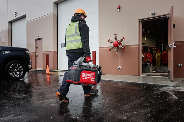 Construction worker carrying a Milwaukee outdoor power tool on a jobsite, highlighting the portability and durability of Milwaukee outdoor power equipment available at Spearfish Building Supply.