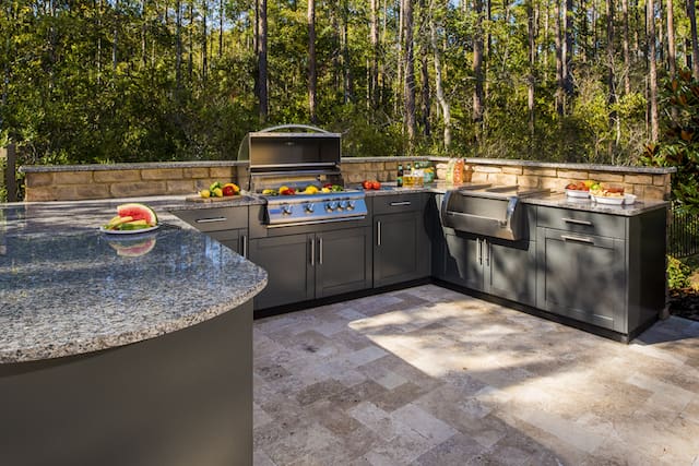 Outdoor kitchen featuring custom gray cabinetry, built-in stainless steel grill, farmhouse sink, and granite countertops—outdoor cabinetry options available at Spearfish Building Supply in Spearfish, SD.